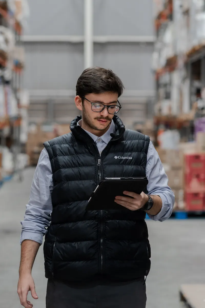 A warehouse coordinator checking stock on a tablet in a warehouse aisle